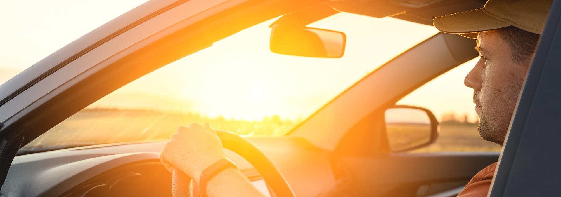 Male driver driving a car at sunset